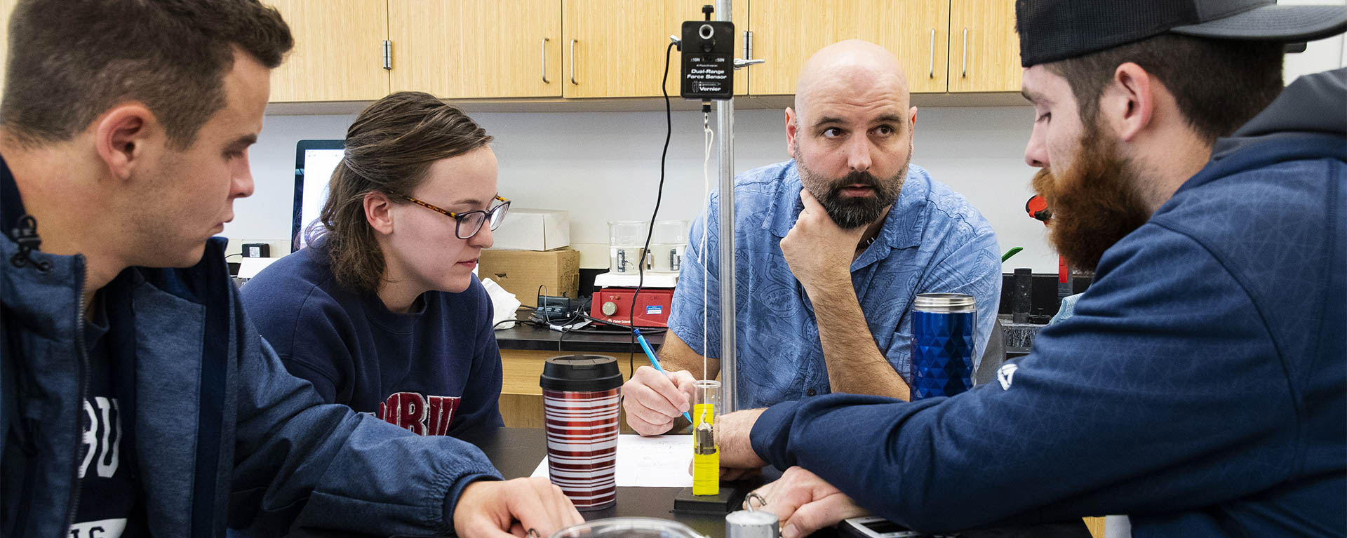 A physics professor and group of students discuss an experiment in the lab.