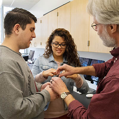 Two students and a professor prepare a beaker for an experiment.