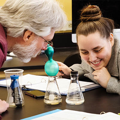 A physics student smiles while watching an experiment in a beaker.