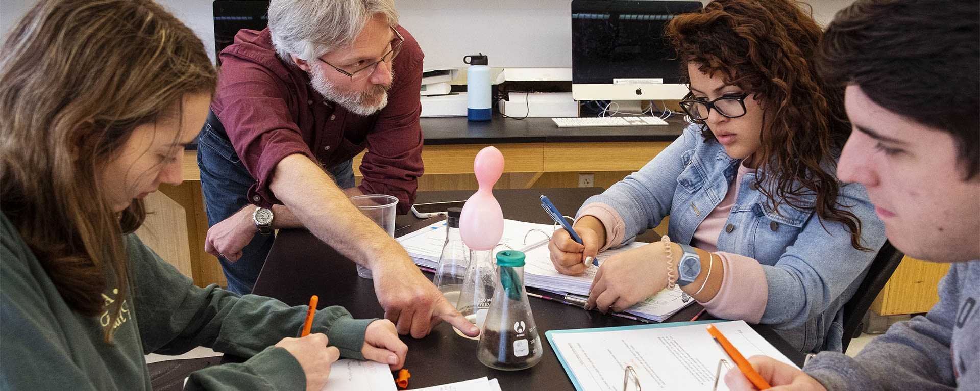 A physics professor and group of students discuss an experiment in the lab.