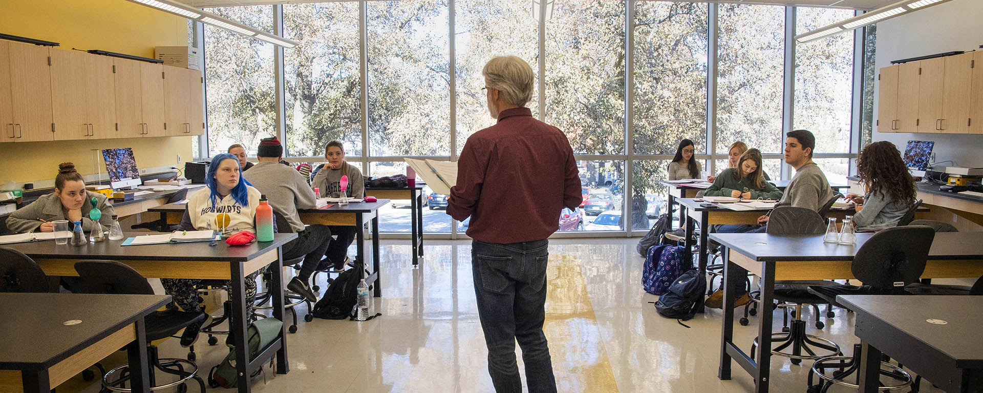 The profile of a professor is seen in front of tables of students focused on what they're teaching.