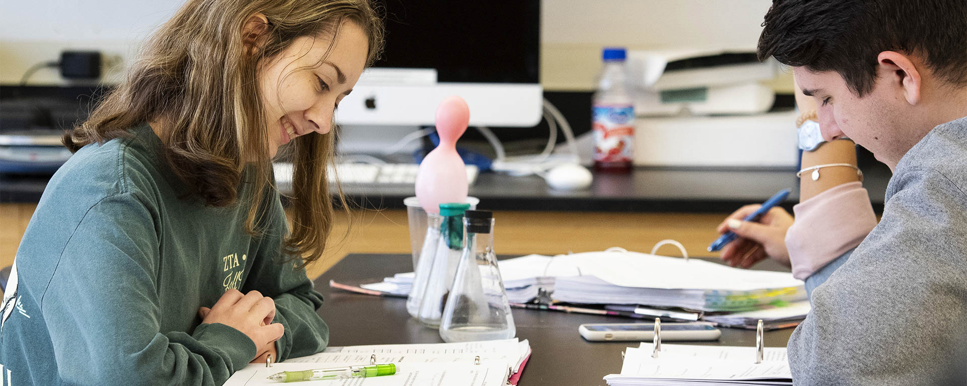 Two students smile while looking at their notes in class.