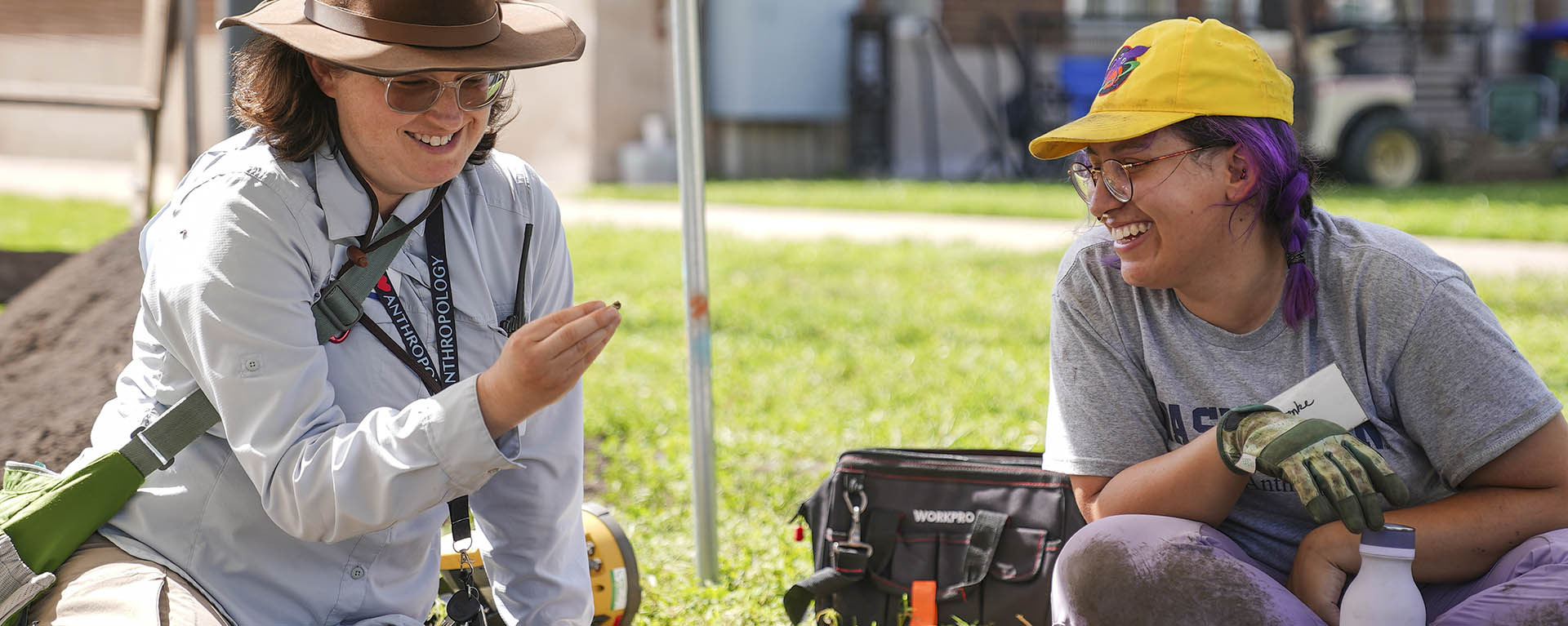 A professor and student smile while examining something they found during an archaeology dig.