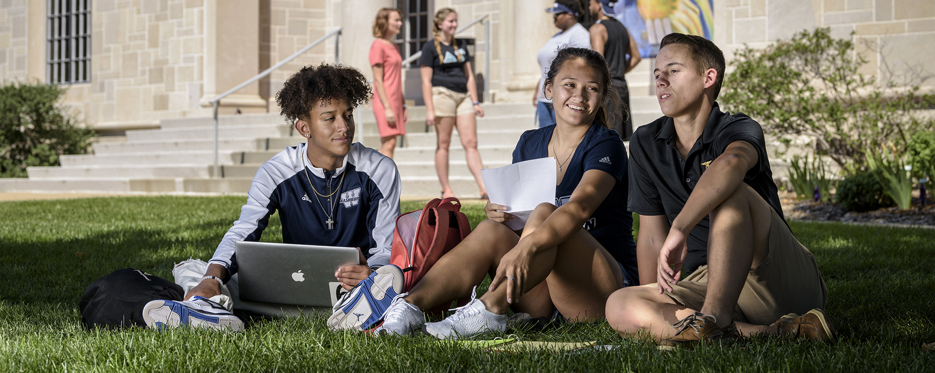 Three Washburn students sit in the lawn in front of the Mulvane Ar Museum.