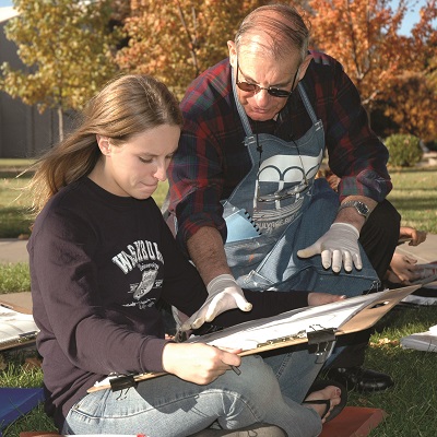 An art professor works with a Washburn student on a painting project.