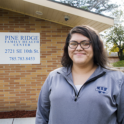 A WTE student smiles in front of a clinic that they are working with.