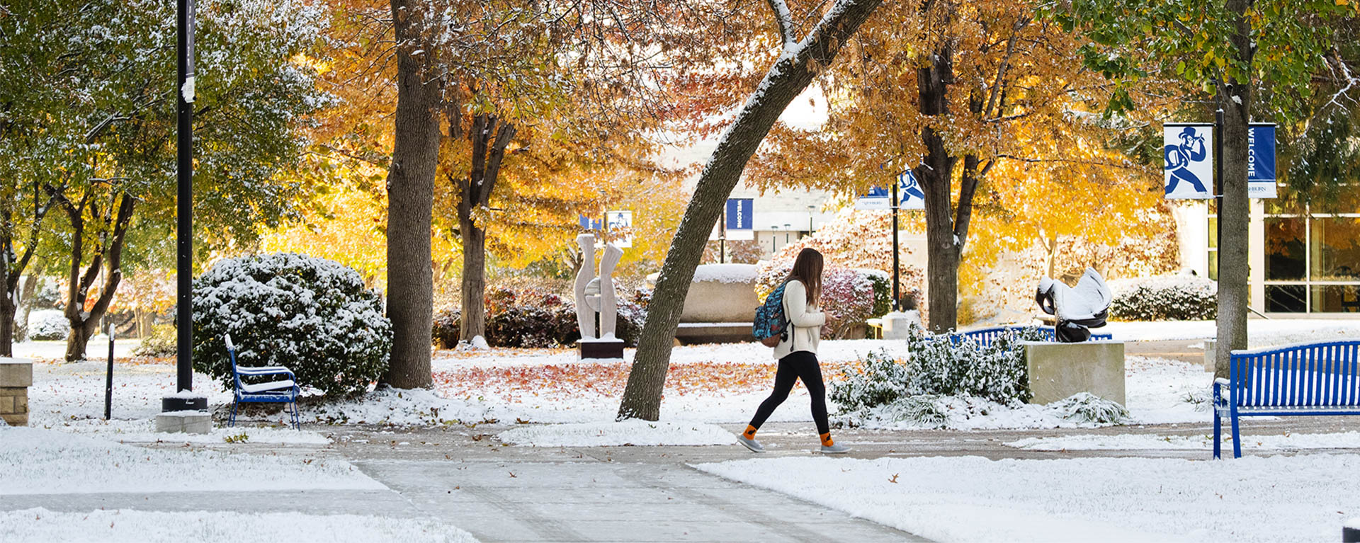 Student walking on campus with fall trees and snow