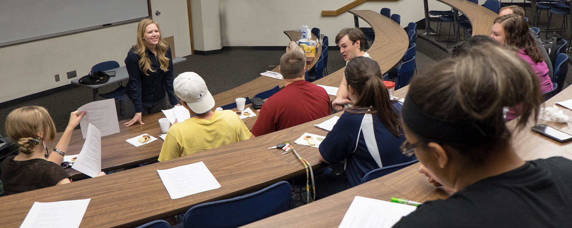 A professor smiles while teaching at the front of a classroom.