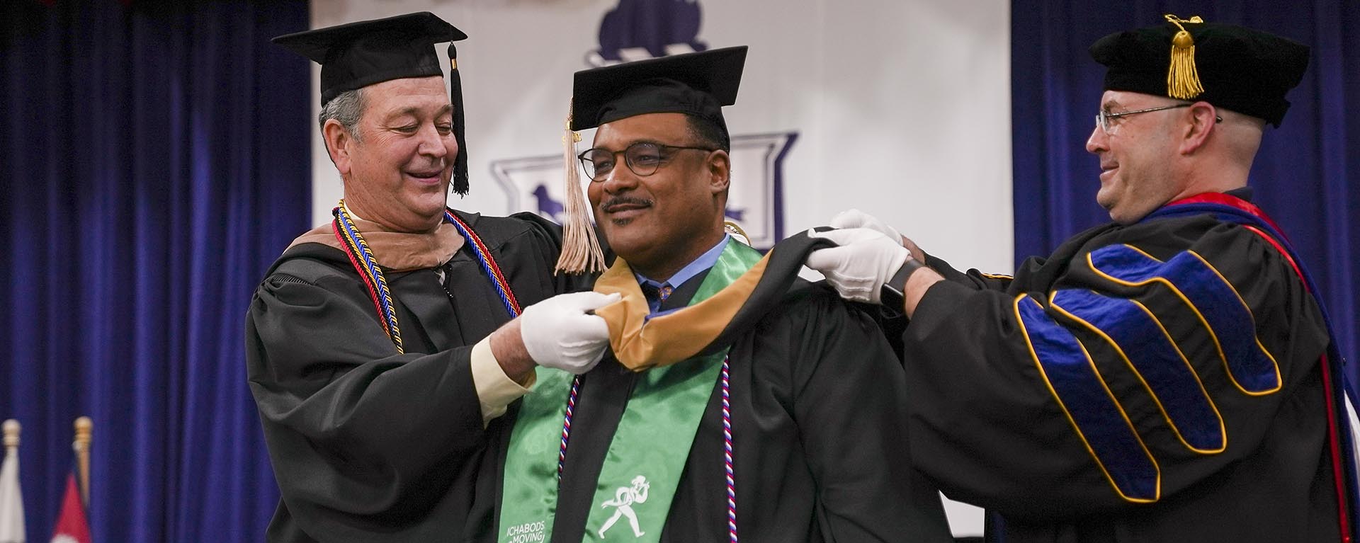 A masters student receives their hood during graduation.