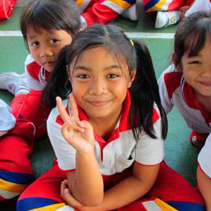 A young girl smiles and holds up a peace sign.