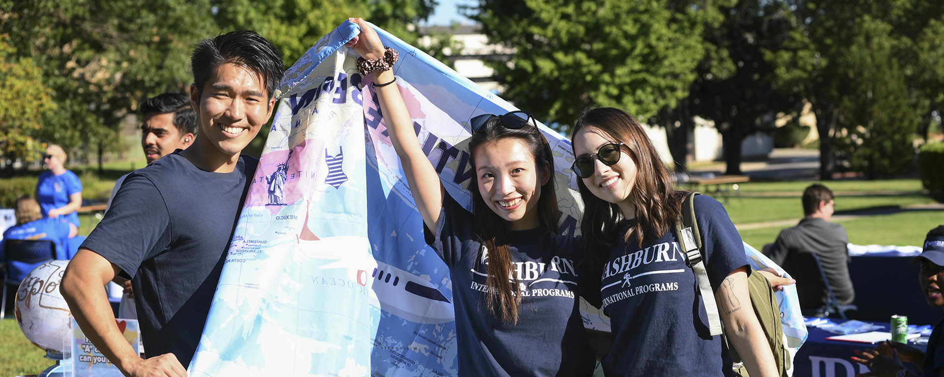 Three international students smile while holding a banner of the world.