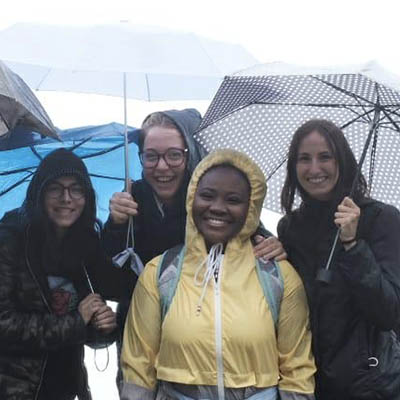 students smile while wearing rain gear and holding umbrellas