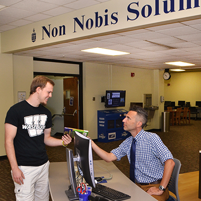 staff member helps smiling student at info desk