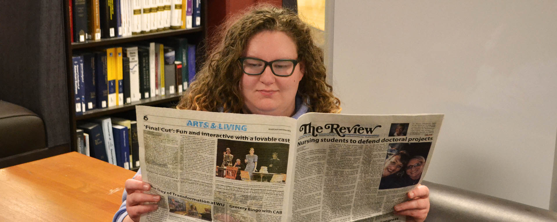 Student in library reading newspaper