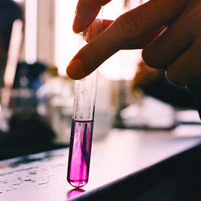 hand holding beaker with pink chemical