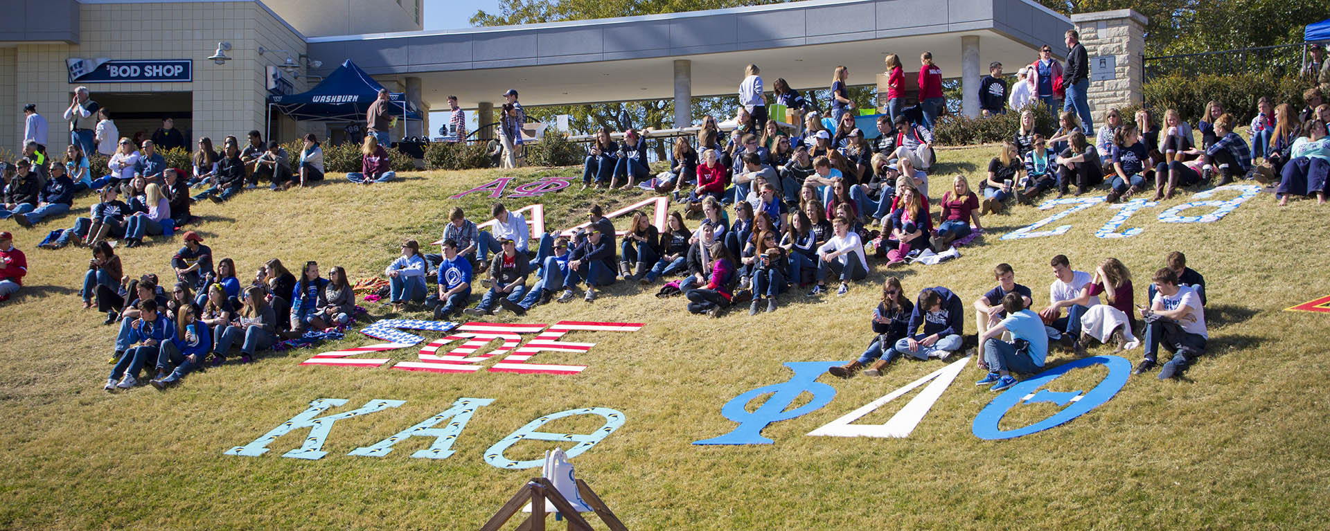 Students with their fraternity and sorority letters sit on the hill to watch the football game.