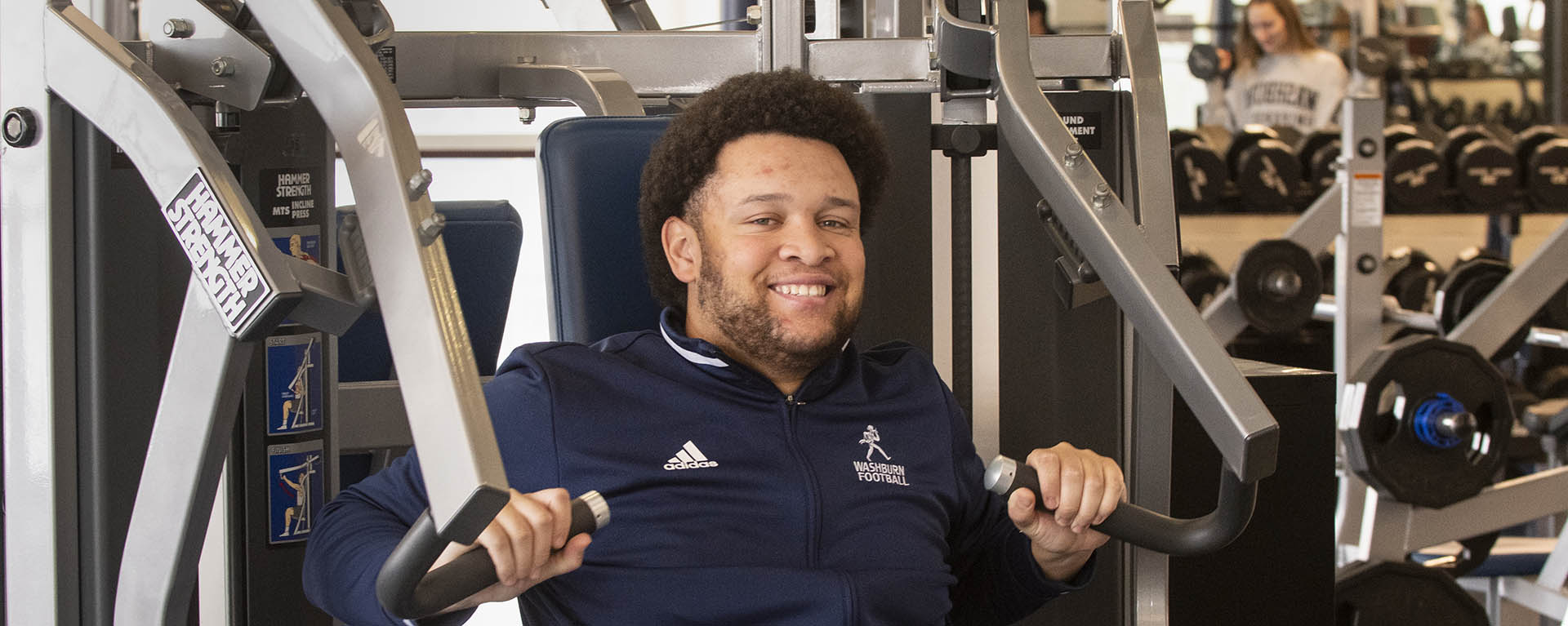 A student smiles while using a strength machine at the Rec center.