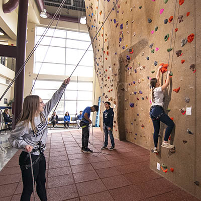 A SRWC employee holds the rope as a student begins climbing the rock wall.