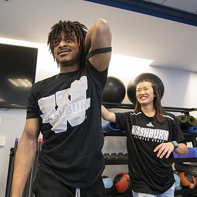A personal trainer helps a student stretch his arm using a band.