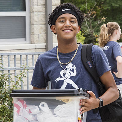 A student smiles while carrying a box on move in day.