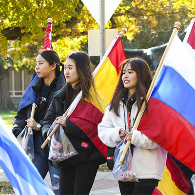 Three students marching in parade, carrying country flags