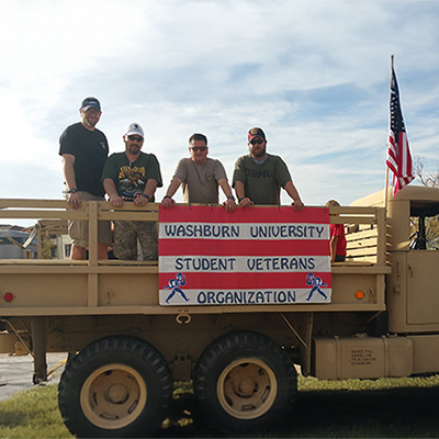military students pose on a truck bed with American flag