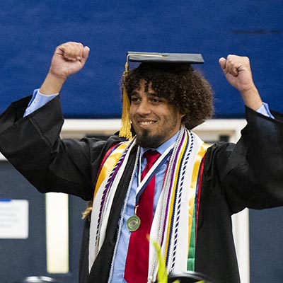 A graduate raises his arms in celebration on stage