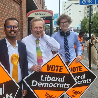 George, right and a two other study abroad trip mates hold signs that say "vote liberal democrat" while in Britain.