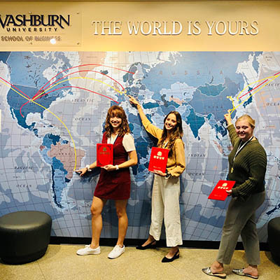 Business students point to a map, showing where they studied abroad.