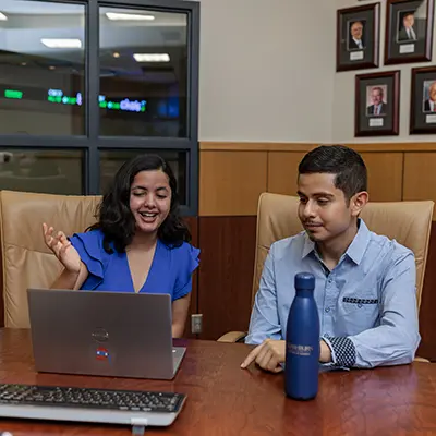 Two students talk about an assignment with a laptop between them.