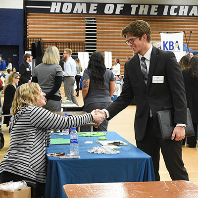 student standing at career fair shaking hands with staff seated at table