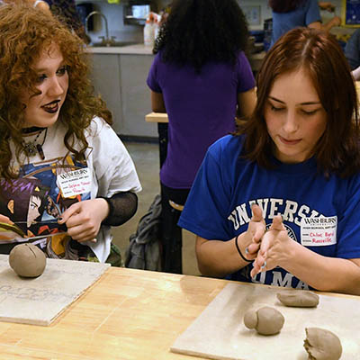 Two students roll out clay during art day.