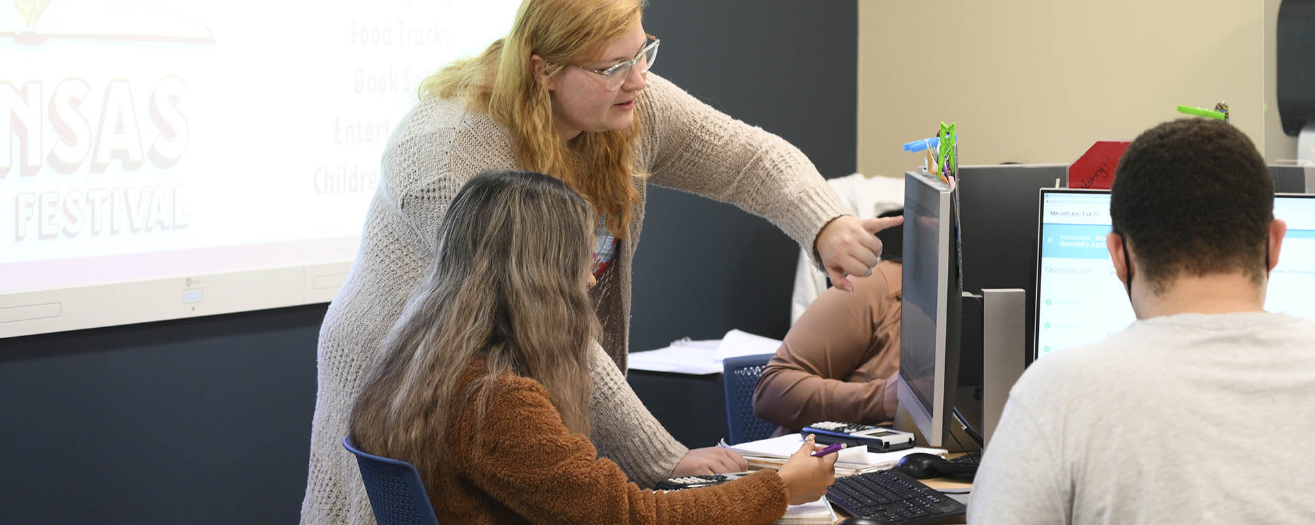 A tutor helps a student with a math problem at a computer.