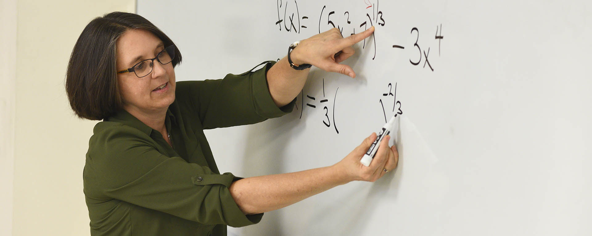 A math professor explains a problem while solving it on a whiteboard.
