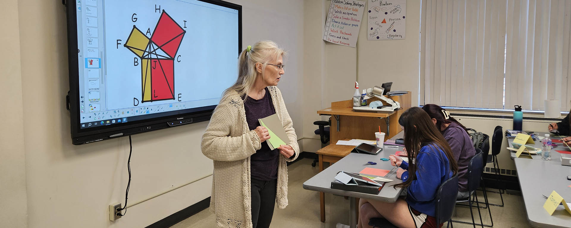 A math professor holds up a triangle on a piece of paper while discussing geometry.