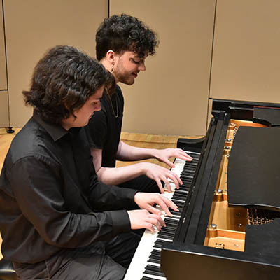 Two students play a piano.