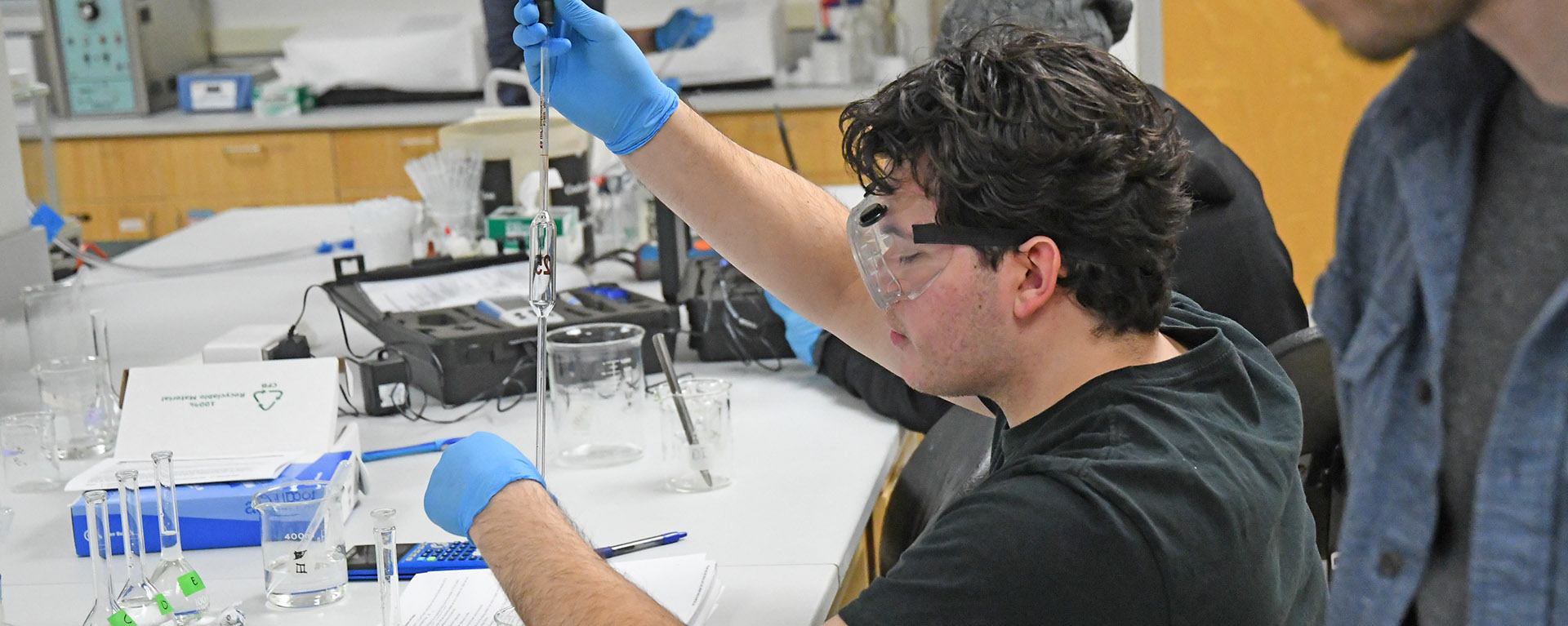 A student wearing goggles performing a science experiment in class.