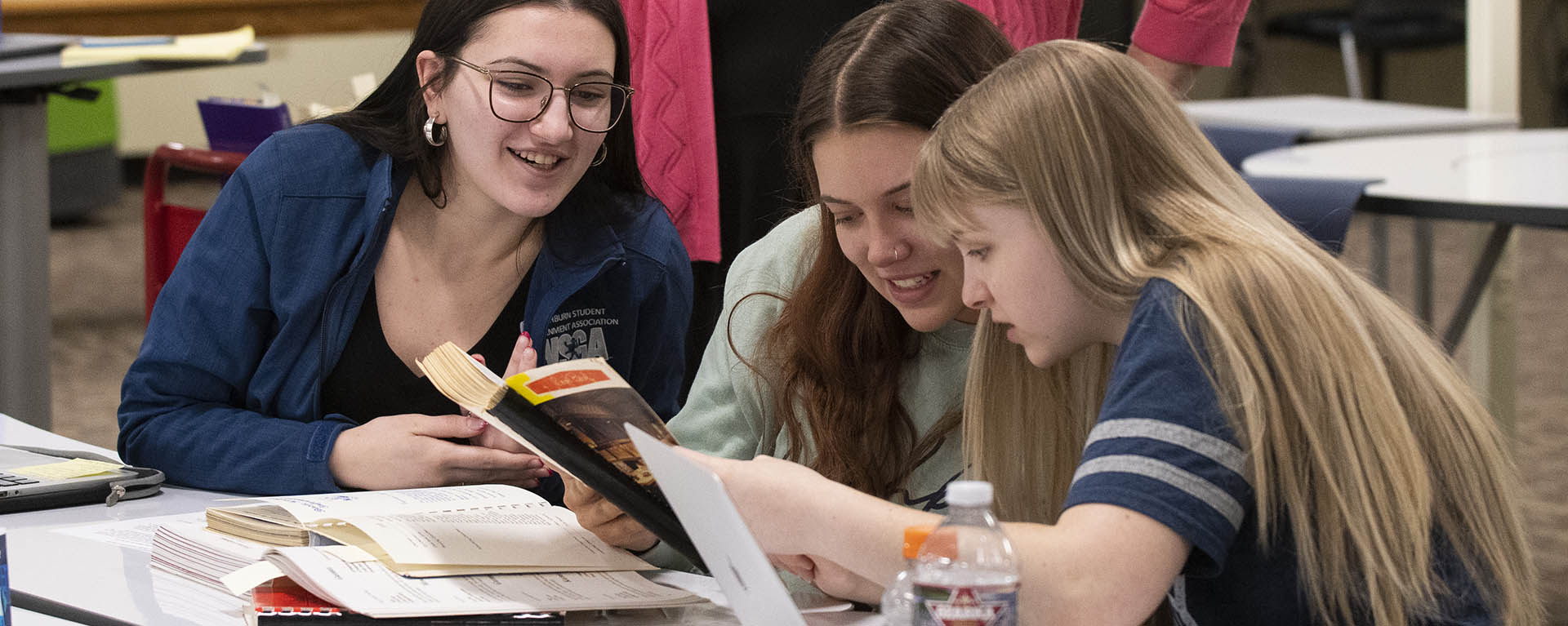 Students smile while looking through old cookbooks for a Sociology project.