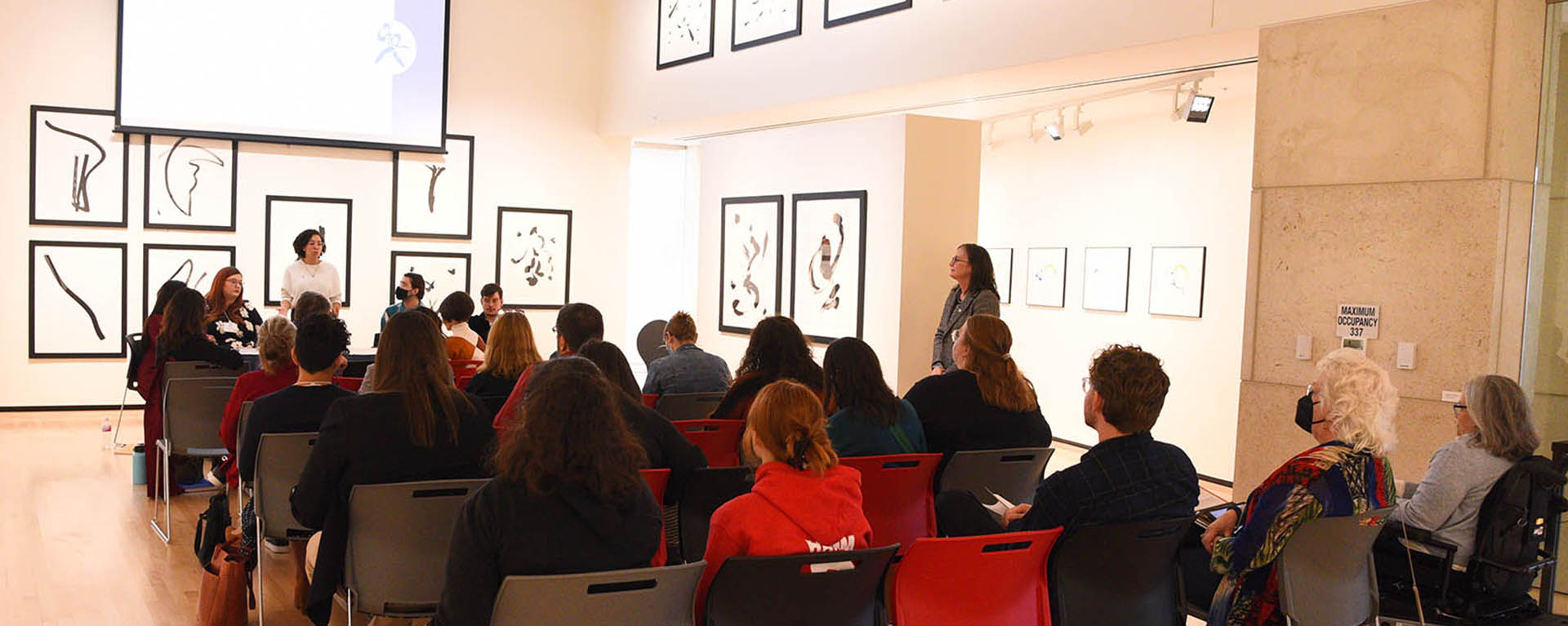 crowd sitting at presentation in art gallery