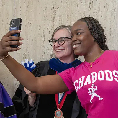 A student takes a selfie with their professor at graduation.