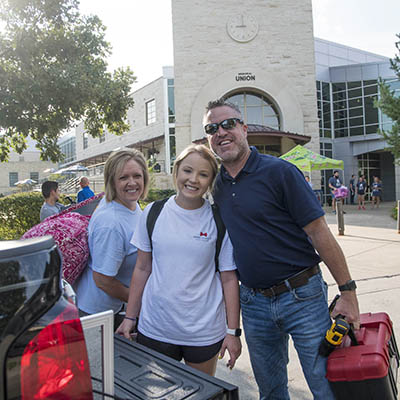 parents smiling with student on campus with luggage