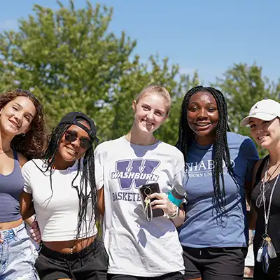 five students standing and smiling with trees and blue sky behind