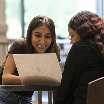 Students smile and look at a computer screen.