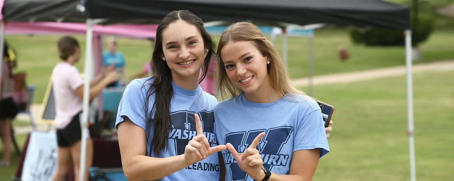 Two Washburn students make a W symbol with their hands while smiling.