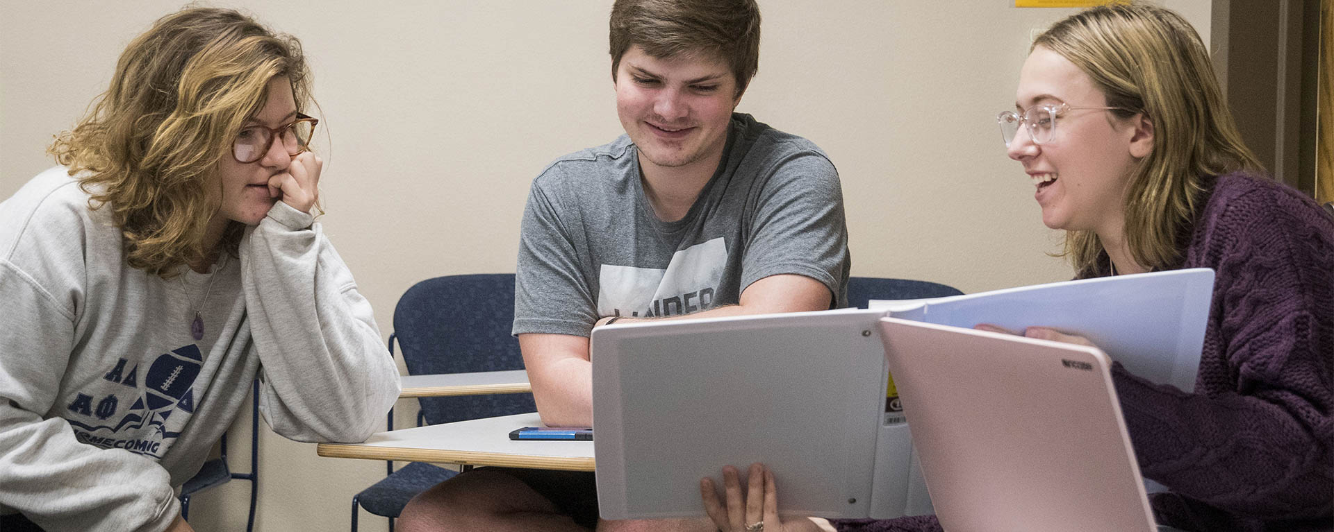 Three students have a discussion while looking at something pointed at in a binder.