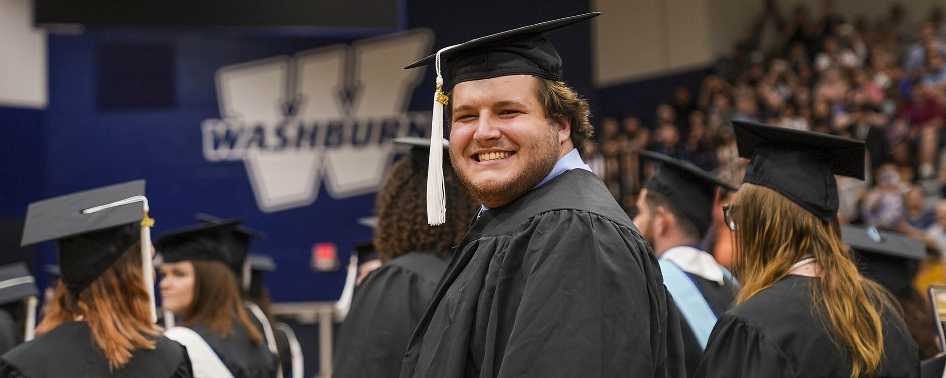 A student smiles widely while wearing graduation regalia. 