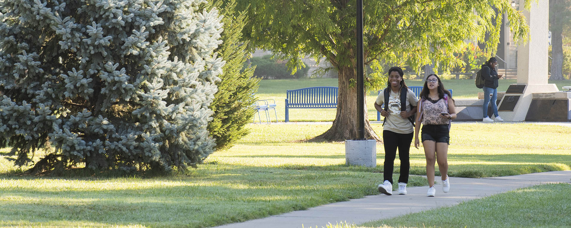 Two students smile and talk while walking to class through the union lawn.