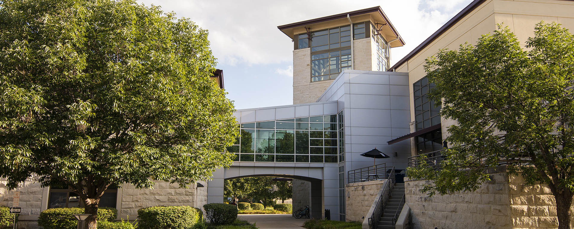 The bridge between the Living Learning Center and Memorial Union spans over a sidewalk on a summer day.