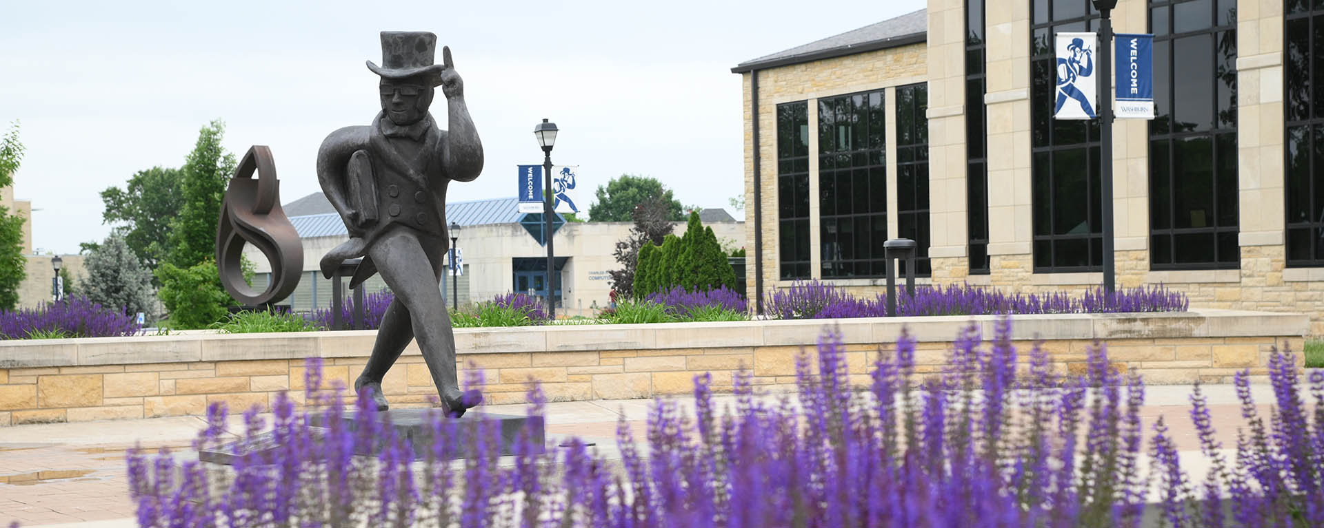 Purple flowers bloom in front of the Ichabod statue at the entrance of Morgan Hall.