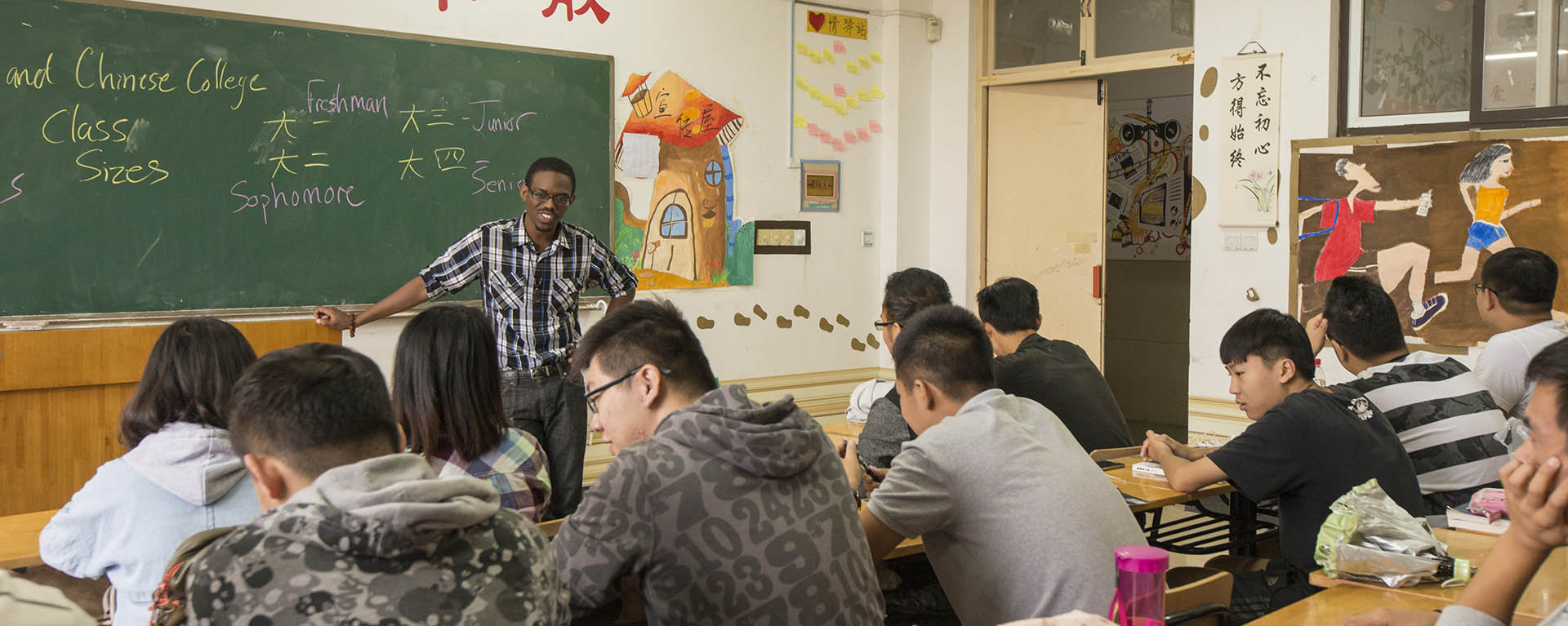 A student gestures towards the chalkboard while teaching a group of students in a Chinese classroom.